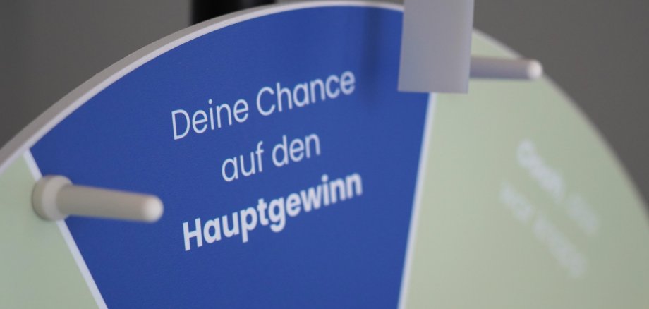 Nahaufnahme eines blau-grünen Glücksrads. Auf einem blauen Segment steht der Text „Deine Chance auf den Hauptgewinn“. Ein Zeiger zeigt auf das Rad. Das Bild wirbt für eine Gewinnspielaktion beim Heimatfest.