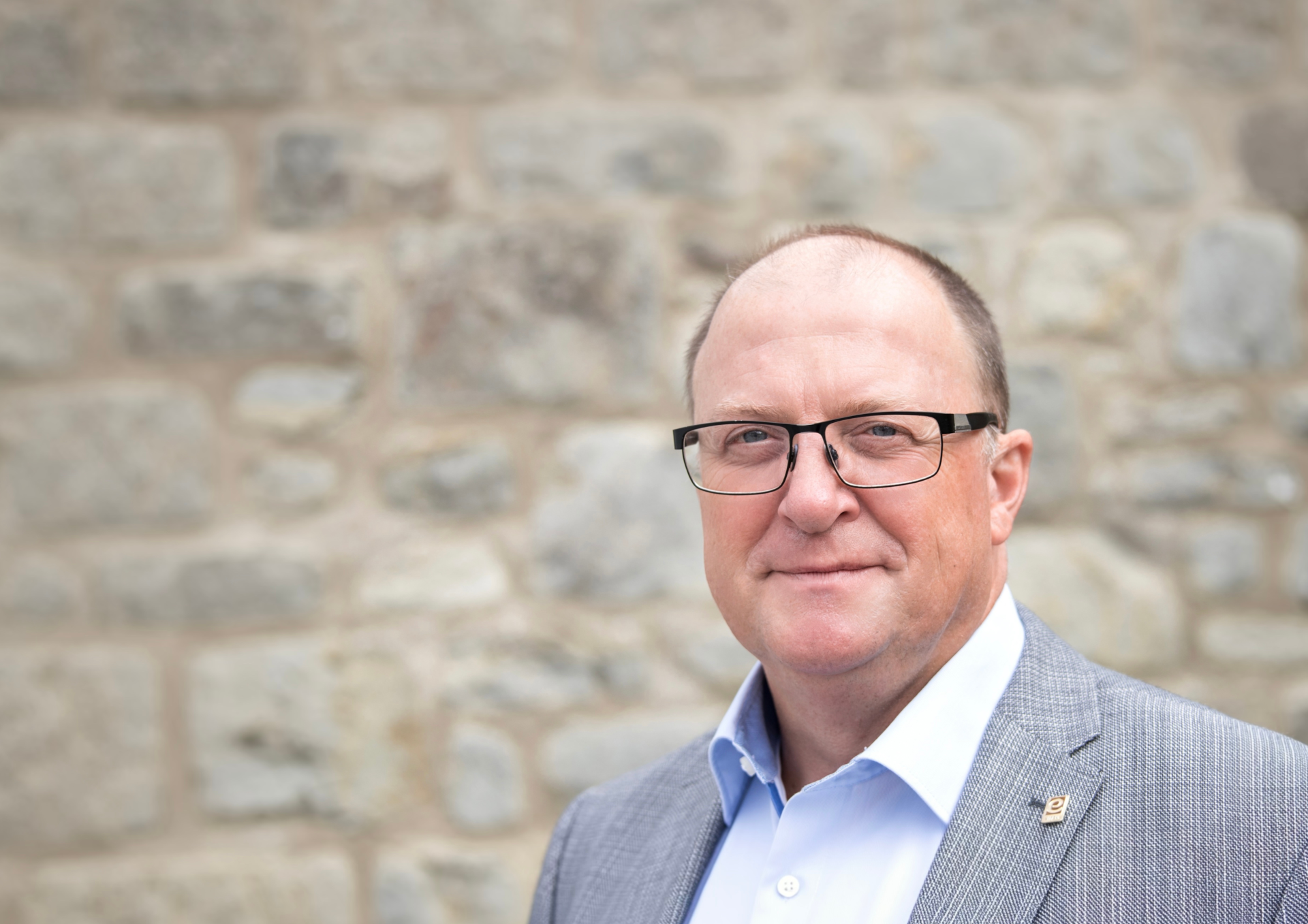 Porträtaufnahme einer Person mit Brille in hellem Sakko und hellblauem Hemd vor einer unscharfen Natursteinmauer. Die Person blickt in die Kamera. Das Foto wird im Zusammenhang mit einer Stellungnahme von Bürgermeister Guido Nisius zu den aktuellen Wald- und Vegetationsbränden verwendet.