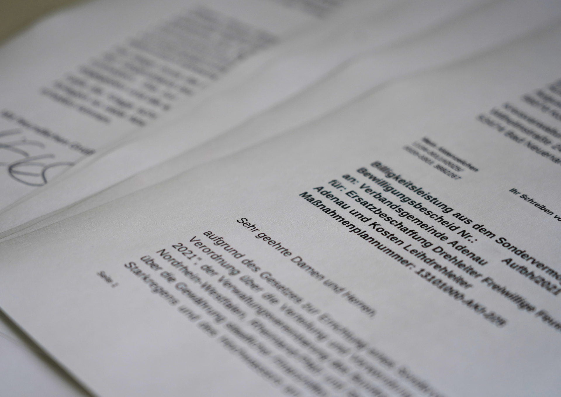 Mehrere Blätter eines offiziellen Dokuments liegen leicht überlappend auf einem Tisch. Das Schreiben trägt den Titel „Bewilligungsleistung aus dem Sondervermögen“ und richtet sich an die Verbandsgemeinde Adenau zur Ersatzbeschaffung einer Drehleiter für die Freiwillige Feuerwehr Adenau.