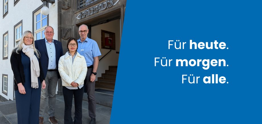 Vier Personen stehen nebeneinander vor einem Verwaltungsgebäude.
