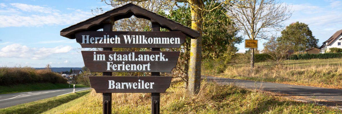 Holzschild am Ortseingang Barweiler mit der Aufschrift Herzlich Willkommen